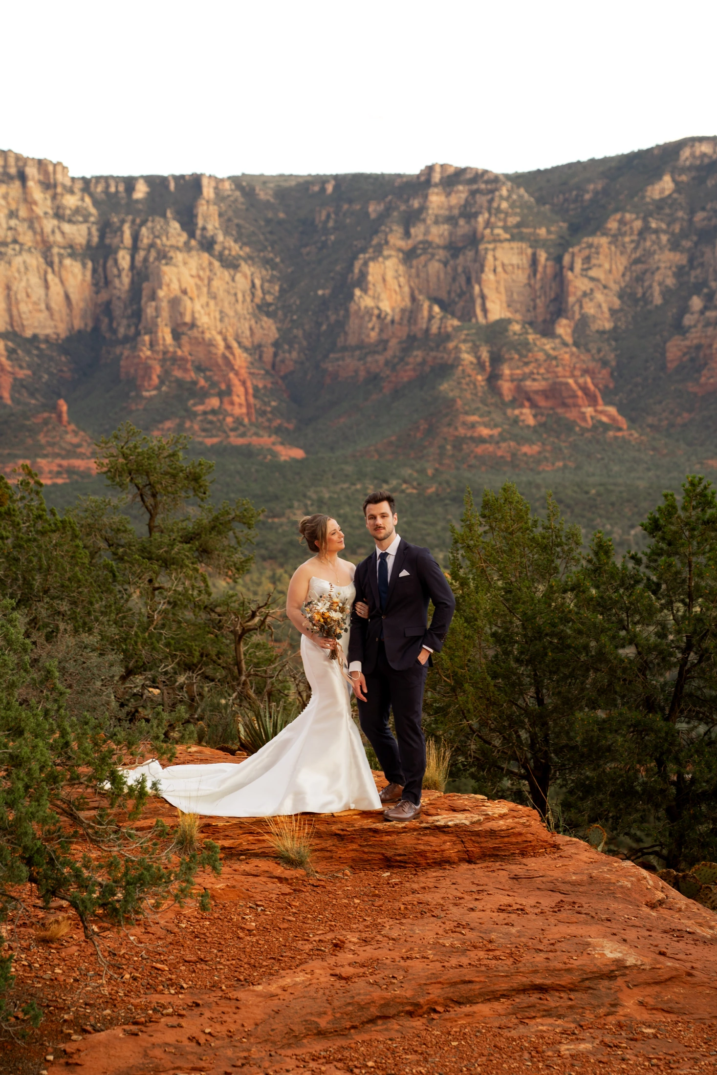 Sheridan and Ayrton together at Airport Mesa, her wedding dress extending across the red rock