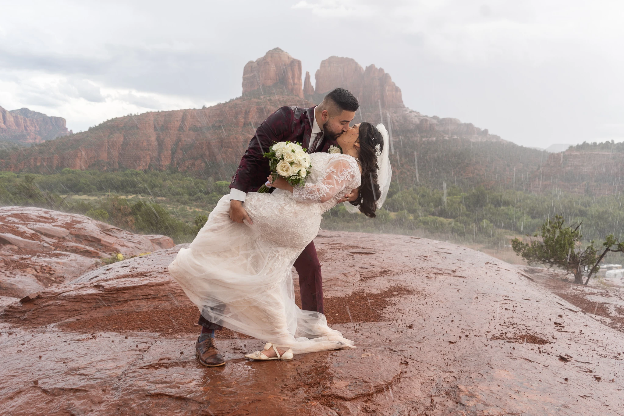A newlywed couple embracing on slickrock with Cathedral Rock in the background